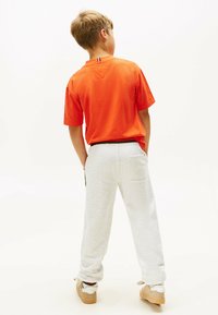 Camiseta de algodón naranja con mangas cortas, combinada con pantalones de chándal gris claro. Los pantalones de chándal tienen bolsillos y un corte relajado.