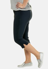 Marineblauwe cropped broek met zijslitsen en een soepele textuur, gecombineerd met zilveren instapschoenen, gepresenteerd op een witte achtergrond.