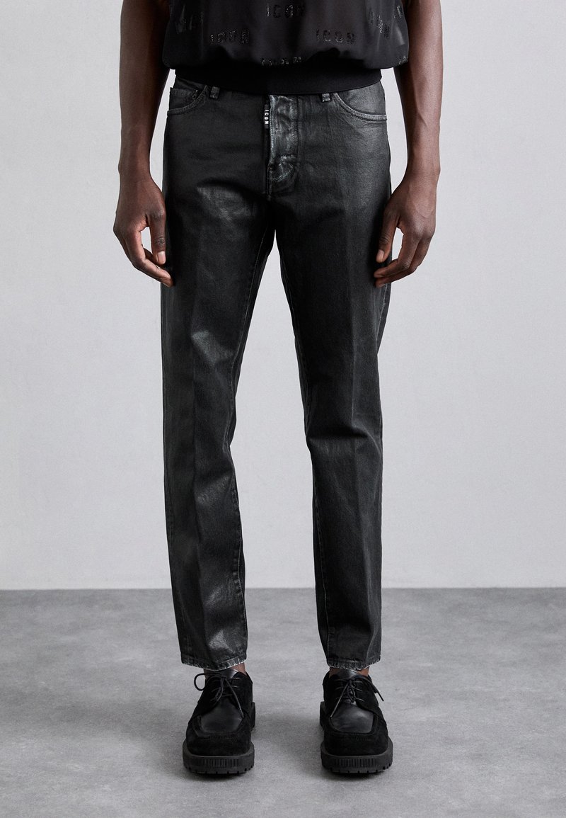Mustad denim püksid, mis on saledalt lõigatud, kerge sädeleva viimistlusega, viie taskuga ja lukuga. Kombineeritud mustade nööridega kingadega.