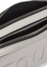 Dwa zamykane na zamek komory w jasnoszarym teksturowanym materiale syntetycznym, wyłożone czarnym materiałem, z metalowymi elementami w kolorze srebrnym i kontrastującymi przeszyciami.
