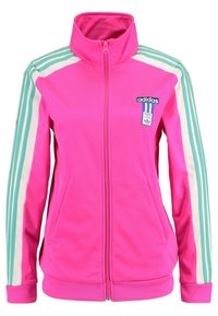 Chaqueta de zip de Adidas en un vibrante color rosa brillante, con rayas de color verde menta y blancas en las mangas y un parche del logo en el lado izquierdo del pecho.
