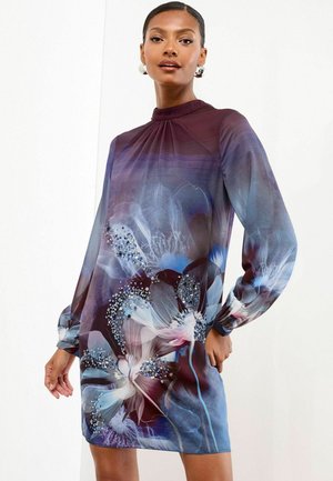 Kukalliset mekko, jossa on korkea kaulus, pitkät hihat ja sekoitus sinisiä ja purppuran sävyjä. Edessä korostettu paljeteilla.