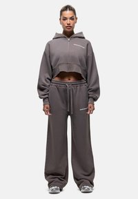 Felpa grigia con zip, taglio cropped, vestibilità rilassata e maniche oversize, abbinata a pantaloni della tuta larghi con cordino, ambos in tessuto morbido.