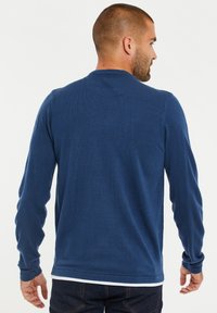 Langarmshirt in Dunkelblau, aus weichem Strickstoff gefertigt. Mit Rundhalsausschnitt und eng anliegenden Ärmeln, verfügt es über eine glatte Textur und minimale Nähte.