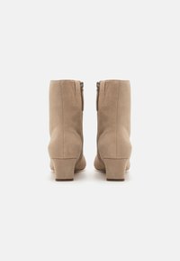 Béžové semišové kotníkové boty s užším podpatkem, zadním zipem a čistým, hladkým povrchem. Detail bočního šití.