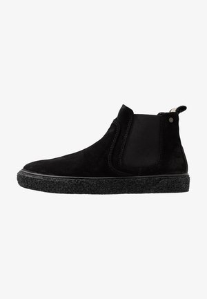 Black suede ankle boots with elastic side panels, textured black rubber sole, and pull tab, featuring smooth and soft materials.