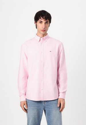 Roze langwerpig overhemd met knopen, gemaakt van katoen, met een puntige kraag, een voorplacket en een klein logo op de borst. G gedragen met blauwe spijkerbroek.