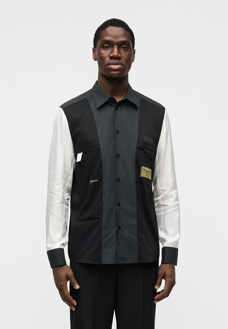 Unisex košile s černou levou stranou a pravou stranou s bílými proužky, s zapínáním na knoflíky, náprsními kapsami a štítky na hrudi.