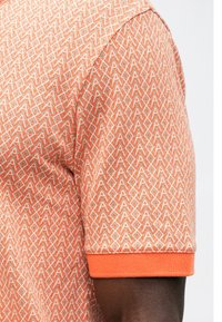 Polo cu mâneci scurte de culoare portocalie, cu un model geometric și garnituri contrastante de portocaliu la mansete, fabricat dintr-un material ușor.