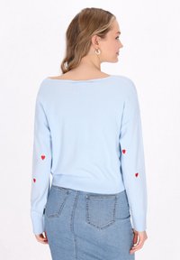 Maglione azzurro chiaro in maglia con scollo ampio e maniche lunghe, caratterizzato da ricami a forma di cuore rosso sulle maniche e un orlo aderente.