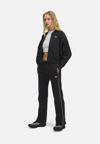 Black athletic set featuring a cropped zip jacket and matching pants. White branding and side stripe detail on pants. Soft fabric.