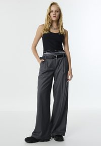 Zwarte tanktop met grijze wijde broek en een zwarte riem. De broek heeft een gestructureerde stof en is gestyled met zwarte schoenen.