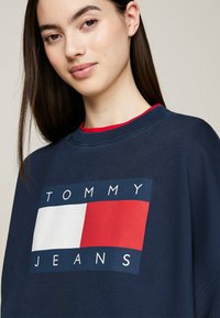 Felpa navy con grande logo caratterizzato da un rettangolo bianco e un quadrato rosso, collo a coste e vestibilità comoda. Il materiale sembra morbido e testurizzato.