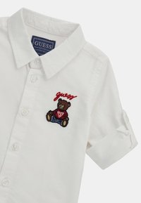 Camicia bianca a maniche corte con un design di orso ricamato con dettagli rossi, colletto a camicia e tessuto di cotone liscio.