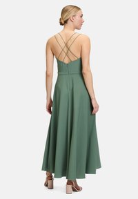 Długa zielona sukienka z gładkiego, lejącego się materiału, z dopasowanym gorsetem, skrzyżowanymi ramiączkami z tyłu i rozkloszowanym dołem.