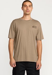 T-shirt marron à manches courtes en coton, avec un col rond et un petit logo noir sur la poitrine gauche. Texture douce, coupe décontractée.