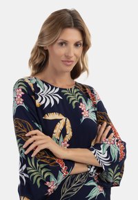 Maglietta blu navy con un motivo floreale tropicale nei toni del verde, rosa e bianco, dotata di maniche a tre quarti a campana e scollatura rotonda.