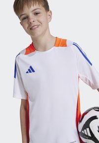 Fehér sporting póló narancssárga és kék kiegészítőkkel, rövid ujjakkal és kerek nyakkal. Az Adidas logóját tartalmazza és egy mintás focilabdát is.