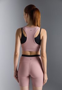 Roze geribbelde sport-bh met zwarte banden en bijpassende roze shorts, met een zwarte tailleband en subtiele logo-detail aan de achterkant.