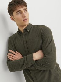 Camisa de botones de manga larga color verde oscuro, hecha de una tela texturizada, con cuello puntiagudo, bolsillo en el pecho y puños con botones.