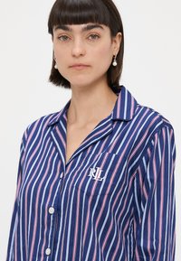 Námořnickomodrý pruhovaný pyžamový vršek s vertikálními růžovými a bílými pruhy, se kapsou s vyšitým logem a knoflíkovým zapínáním.