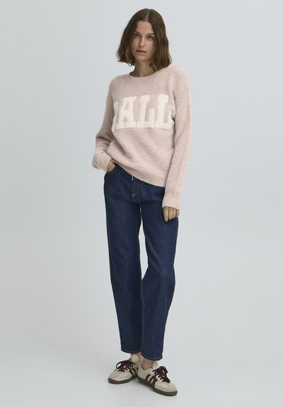 Šviesiai rožinė megzta palaidinė su baltais "HALL" rašmenimis, derinama su tamsiai mėlynomis tiesiomis kelnėmis ir kreminiais sportbačiais su burgundiškais akcentais.