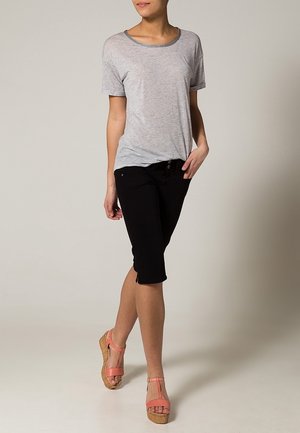 Camiseta gris de manga corta con cuello redondo a rayas, combinada con pantalones capri negros y sandalias de cuña rosas con plataforma trenzada.