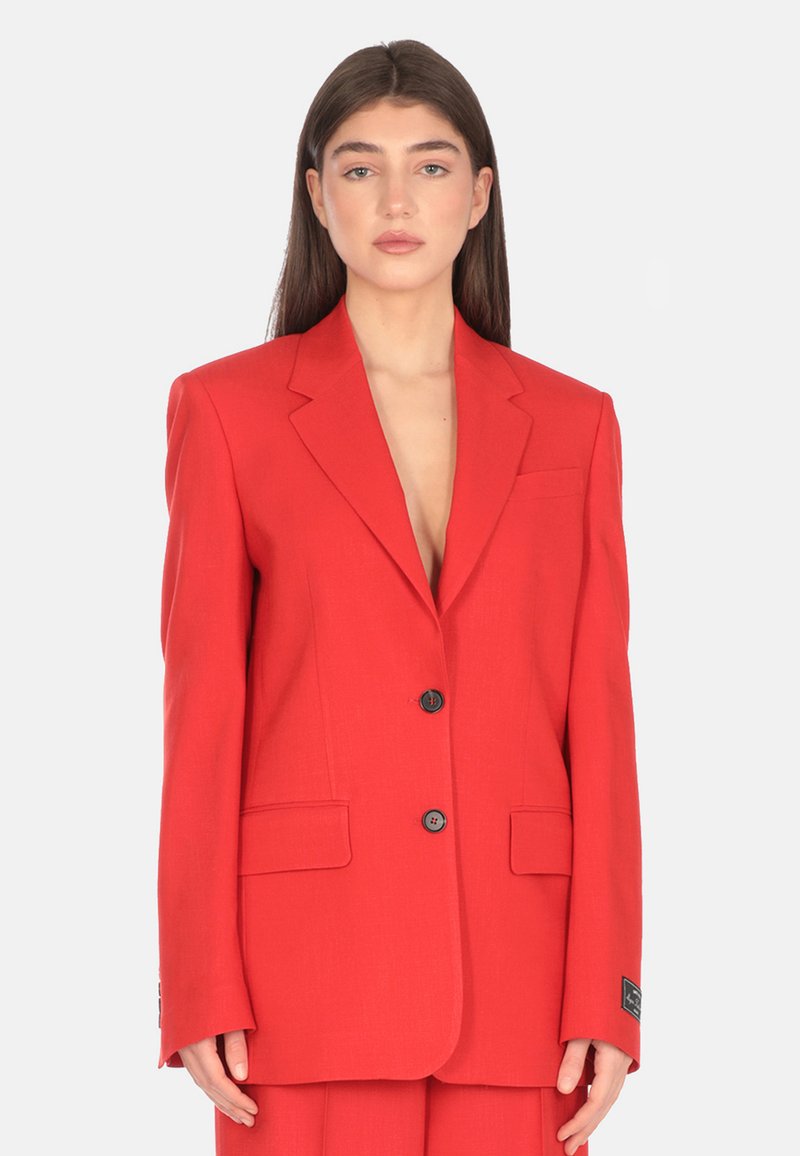 Blazer rosso con una vestibilità su misura, revers a punta, due bottoni e tasche laterali. Realizzato in tessuto leggero con una consistenza liscia.