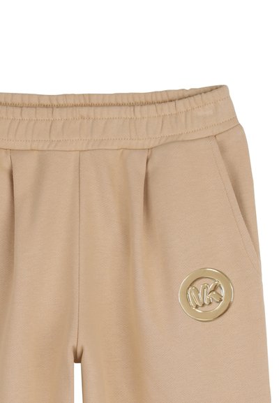 Pantalon jogger beige en tissu lisse, doté d'une ceinture élastique, de deux poches avant et d'un logo doré sur la hanche.