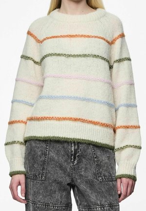 Suéter blanco de punto con rayas difusas horizontales en naranja, verde, rosa y azul, combinado con jeans negros desteñidos de talle alto.