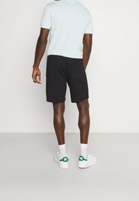 Pantalones cortos negros de algodón con un ajuste relajado, combinados con una camiseta de color azul claro. Zapatillas blancas con detalles en verde y calcetines blancos.