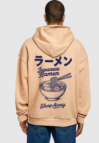 Sudadera color beige con un gráfico en azul marino de un tazón de ramen con fideos y huevos, texto en japonés e inglés, corte relajado.