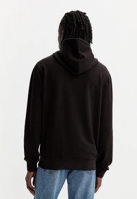 Zwarte sweatshirt met capuchon, in een relaxte pasvorm, met lange mouwen en ribgebreide manchetten. Het materiaal lijkt zacht, met minimale zichtbare naden.