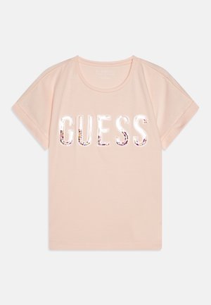 T-shirt in cotone rosa chiaro con maniche corte, decorata con un logo "GUESS" in un carattere audace, impreziosita da paillettes. Collo rotondo, vestibilità casual.