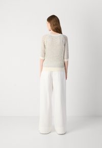 Gebreide trui in lichtbeige met een losse, gestructureerde ontwerp, driekwart mouwen en een crèmekleurige zoom. Gecombineerd met witte, wijd-uitlopende broeken.