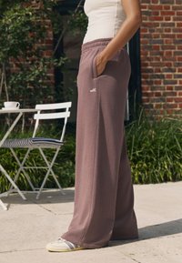 Pantaloni de trening lejeri, de culoare mov pal, cu buzunare laterale, talie elastică și logo-ul „self.”. Asortați cu adidași de culoare deschisă și un maiou.