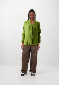 Green textured blazer with two buttons, paired with brown wide-leg pants and black and white sneakers. Simple silver jewelry accents.