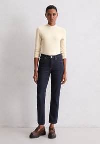 Beige getailleerde shirt met lange mouwen, donkerblauwe high-waisted jeans en bruin veterschoenen met een dikke zool. Eenvoudig ontwerp en klassieke pasvorm.