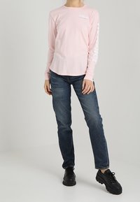 Camicia a maniche lunghe rosa chiaro con scollo rotondo. Jeans blu e sneakers nere con suola spessa completano l'outfit. Design semplice, senza motivi.
