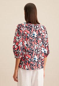Bluzka w kwiatowy wzór w różowym, granatowym i białym kolorze. Luźny fason z bufiastymi rękawami i zaokrąglonym dołem. Lekka tkanina o gładkiej strukturze.
