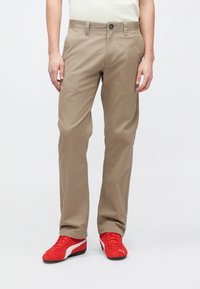Μπεζ βαμβακερές chino παντελόνια με ίσια γραμμή, με κλείσιμο με κουμπί και πλαϊνές τσέπες. Συνδυασμένα με κόκκινα παπούτσια Puma.