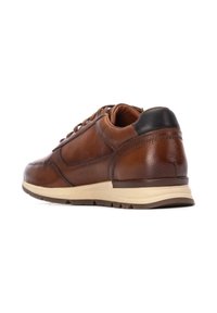 Zapatilla de cuero marrón con un perfil bajo, puntera redondeada y talón negro contrastante. Presenta detalles de costura y una suela de color claro.