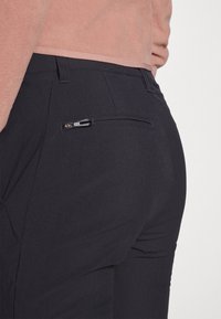 Schwarze Hosen mit einer glatten, matten Textur, ausgestattet mit einer Reißverschluss-Gesäßtasche und einer taillierten Passform. Der Bund ist zur besseren Komfort verstellbar.