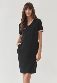 Black short-sleeve dress with a V-neck, featuring contrasting beige trim on sleeves and neckline, along with side pockets. Smooth texture.