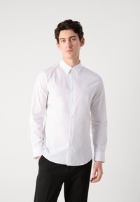 White long-sleeve shirt with a classic collar, button-front, and subtle logo. Smooth cotton fabric with a fitted design and curved hem.
