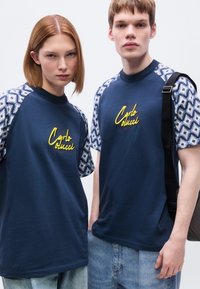 Μπλε ναυτικό μπλουζάκια με κοντά μανίκια με σχέδιο, με το κέντημα «Carlo Colucci» σε κίτρινο. Ευθεία γραμμή, βαμβακερό ύφασμα, casual σχεδίαση.