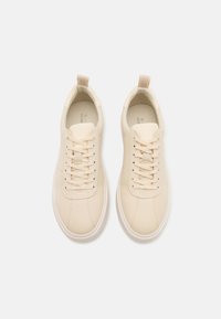 Cream-colored leather sneakers with a smooth texture, round toe, flat laces, and a small pull tab at the heel. Casual design.