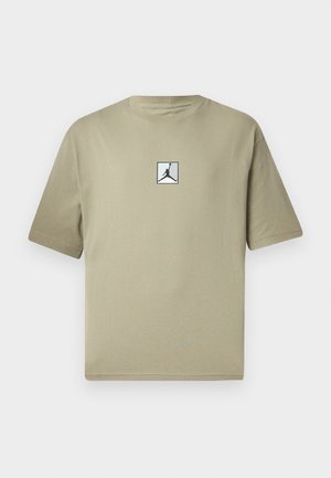 Khakifarbene Baumwoll-T-Shirt mit kurzen Ärmeln, das auf der Vorderseite ein kleines schwarzes Jordan-Logo in einem weißen Quadrat zeigt. Einfaches Design und lockere Passform.