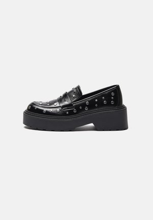 Zwarte leren loafer met een dikke plateauhak en zilveren studs als versiering op de bovenkant en zijkanten, zijaanzicht.