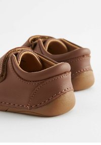 Chaussures en cuir marron avec une texture lisse, bout arrondi et couture contrastante. Semelle souple et basse, avec un col légèrement rembourré.